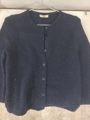 Mörkblå fluffig kofta Gina Tricot  - Mysig mörkblå kofta från Gina Tricot med fluffig känsla. Rund halsringning, knäppning framtill med sju knappar och lång ärm. Perfekt för lager-på-lager och enkel att styla till olika outfits.