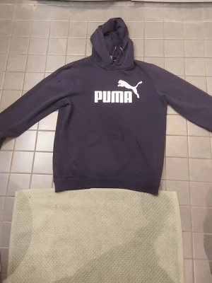 Mörkblå hoodie från Puma - Snygg mörkblå hoodie från Puma med stor vit logga och text på bröstet. Klassisk huva med snörning och mjukt material som känns skönt mot huden. Perfekt för dig som gillar sportig och avslappnad stil. kan skickas eller mötas upp, skriv om ni har några frågor