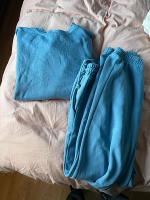 Blått loungewear-set från Zara - Mysigt blått loungewear-set från Zara med matchande sweatshirt och byxor. Setet är tillverkat i mjukt material med borstad insida för extra komfort. Byxorna har resår i midjan och tröjan har rund halsringning. Perfekt för chill dagar hemma. Noppror finns, se bilder 