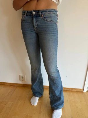 Blå bootcut jeans från Lager157 - Säljer ett par klassiska blå low bootcut jeans från Lager157 med fem fickor. Jeansen har en snygg tvättad look och är tillverkade i denim med lätt stretch för skön passform. Perfekta för en avslappnad och trendig stil. Lite slitna i hälen.