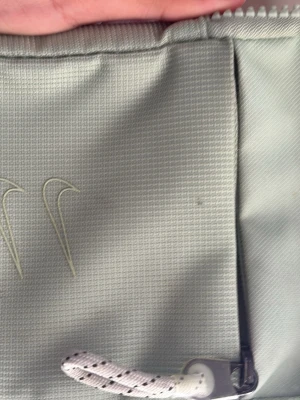 Ljusgrön Nike axelväska med logga - Axelväska i ljusgrönt från Nike med två broderade swoosh-loggor på framsidan. Väskan har justerbar axelrem med stor NIKE-text i vitt och svart. Materialet är slitstark textil med rutmönstrad struktur och dragkedja med repdetalj.