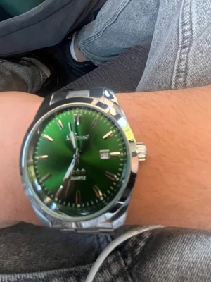 Grön klocka + plus Klockarmbandsverktyg - Snygg klocka  grön urtavla och datumvisning. Klockan har en klassisk rund form och en länk i silverfärgat stål som ger en clean och modern look. Perfekt accessoar för dig som vill sticka ut lite extra.