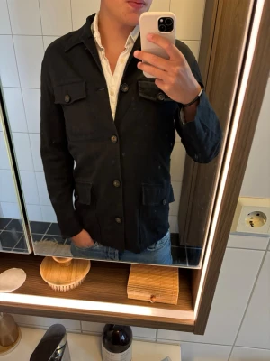 Svart jacka från Rykiel Homme - Stilren svart jacka från Rykiel Homme med klassisk krage och flera fickor framtill. Jackan har knäppning med knappar och en rak passform som passar till många olika outfits. Perfekt för dig som vill ha en snygg och enkel look.