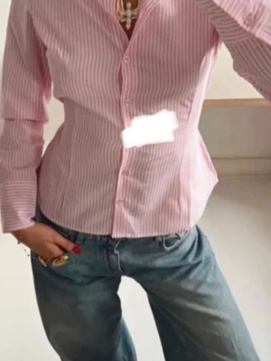 Rosa och vit randig skjorta - Säljer en snygg rosa och vit randig skjorta med klassisk krage och knappar framtill. Skjortan har lång ärm och en figurnära passform som ger en clean och fräsch look. Perfekt att styla till jeans eller kjol för en trendig outfit.