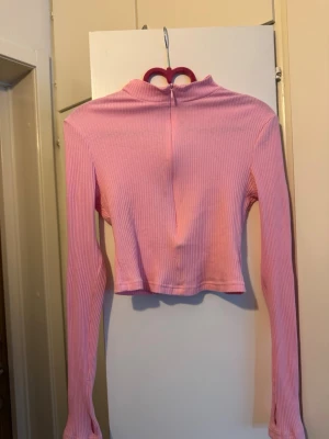 Topp rosa strl S - Långärmad topp i ribbat tyg med hög krage och dragkedja framtill. Toppen är croppad och har muddar med tumhål.
