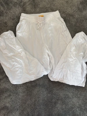 Vita linnebyxor  - Säljer ett par vita linnebyxor med avslappnad passform och resår i midjan samt dragsko för justerbar komfort. Byxorna har raka ben och är perfekta för en chill och stilren look. Materialet är lätt och luftigt linne.