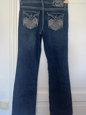 Mörkblå bootcut jeans Code Bleu/stylowe jeansy z kieszeniami - Snygga mörkblå bootcut jeans från Code Bleu med kontrastsömmar och detaljerade bakfickor med broderi och knappar. Klassisk femficksmodell i kraftigt denimtyg, perfekta för en avslappnad men trendig look.