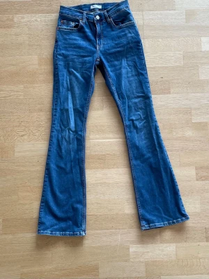 Blå bootcut jeans med utsvängda ben - Säljer ett par klassiska blå bootcut jeans med utsvängda ben, normal midja och femficksmodell. Perfekta för dig som gillar retrostil och vill ha ett par jeans som sticker ut lite extra.