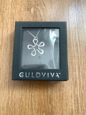 Guldviva silverhalsband blomma - Snyggt halsband från Guldviva i silver med ett unikt blomformat hänge. Kedjan är tunn och stilren, och hänget har en modern, organisk design som verkligen sticker ut. Perfekt accessoar för att lyfta vilken outfit som helst.