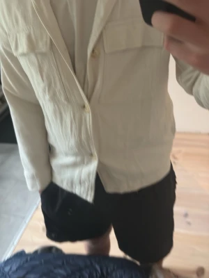 Ljusbeige overshirt med fickor - Stilren ljusbeige overshirt med två bröstfickor och knäppning framtill. Skön, lite strukturerad bomullskänsla och avslappnad passform. Perfekt att slänga över en t-shirt för en clean look.