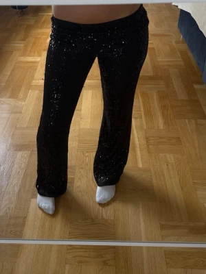 Svarta paljettbyxor med bootcut - Glittriga svarta byxor med paljetter och bootcut-modell. Perfekta för att sticka ut och ge extra bling till din outfit. Byxorna är använda en gång och är i super bra skick.