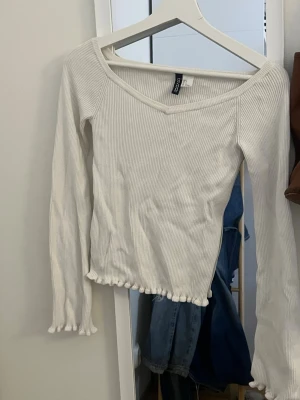 Vit ribbad topp från Gina Tricot - Säljer en vit långärmad topp från Gina Tricot med ribbad struktur och v-ringning. Toppen har volangkant vid ärmslut och nederkant för en söt touch. Tillverkad i mjukt stretchigt material som sitter snyggt på kroppen.