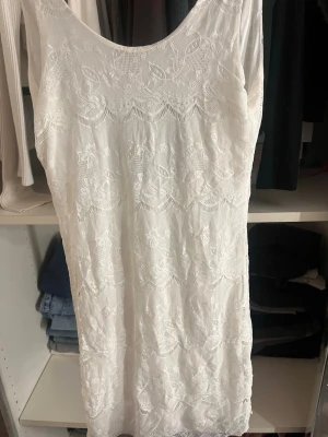 Vit spetsklänning med öppen rygg  - Säljer en vit kort klänning i spets med vackert blommönster. Klänningen har en djup rygg, vilket ger en luftig och somrig känsla. Perfekt för varma dagar eller speciella tillfällen. Materialet känns lätt och mjukt mot huden. Kort och tajt klänning
