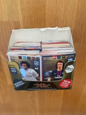 FIFA 365 Adrenalyn XL samlarkort 2017 - Stor samling FIFA 365 Adrenalyn XL samlarkort Nordic Edition från 2017 i original kartong. Det finns runt 400-500 kort i denna kartong.    Korten har färgstarka tryck med olika fotbollsspelare och lag, och boxen är svart, vit och guld med tydliga FIFA 365 och Panini-loggor. Perfekt för dig som gillar fotboll och samlarkort.