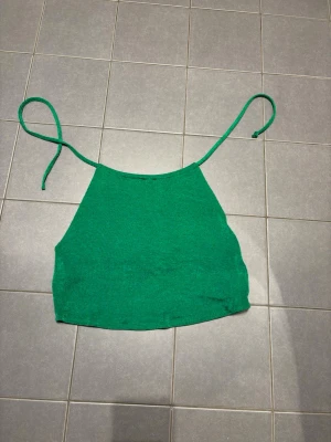 Grön croppad linnetopp - Snygg grön croppad linnetopp med tunna axelband som knyts. Perfekt till sommaren och enkel att matcha med jeans eller kjol. Toppens material känns mjukt och lätt, vilket gör den skön att bära under varma dagar.