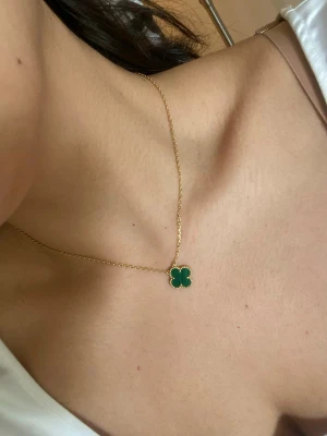 Guldhalsband med grön fyrklöver halvädelsten - Snyggt halsband i guld med en grön fyrklöverformad berlock. Kedjan är tunn och elegant, och berlocken har guldfärgade kanter som ger en exklusiv känsla. Perfekt för dig som gillar stilrena och trendiga smycken med en touch av färg.
