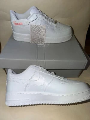 Nike Air Force 1 vita sneakers - Klassiska helvita Nike Air Force 1 sneakers i lågt utförande. Skorna har en clean design med vit sula, vita skosnören och den ikoniska swoosh-loggan på sidan. Tillverkade i slätt läder för en stilren look. Perfekta för dig som gillar tidlös streetstyle.
