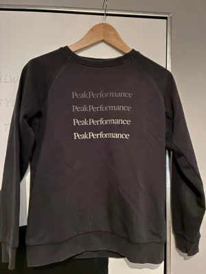 Svart sweatshirt Peak Performance - Svart sweatshirt från Peak Performance med tryckt logga i flera storlekar på bröstet. Tröjan har rund halsringning, ribbade muddar vid ärmslut och nederkant samt en klassisk, avslappnad passform. Perfekt för en casual och sportig stil. Storlek 160
