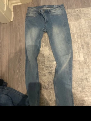 Blå slim fit jeans med slitningar - Snygga blå slim fit jeans med lätt slitna detaljer och klassisk femficksdesign. Jeansen har en något tvättad look och smal passform som sitter tajt längs benen. Perfekta för en avslappnad och trendig stil.