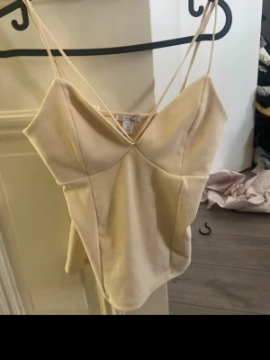 Beige linnetopp med smala axelband - Snygg beige linnetopp med smala axelband och v-ringad hals. Toppen har figurnära passform och är perfekt för varma dagar. Enkel och stilren design som passar till mycket.