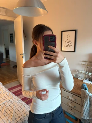 Vit ribbad offshoulder topp - Trendig vit ribbad topp med offshoulder-design och långa ärmar. Sitter tight (på mig iallafall) och har en bred kant över axlarna som ger en snygg siluett. Perfekt att styla med jeans eller kjol för en clean look. Finns några noppor.