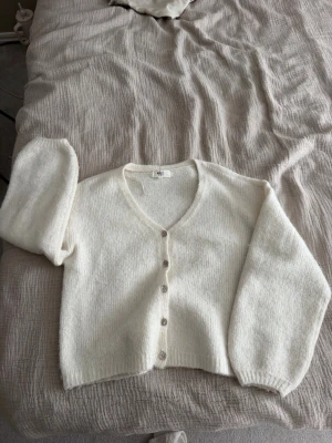 Vit kofta från Gina Tricot - Mysig vit kofta från Gina Tricot i ullblandning. Koftan har v-ringning, långa ärmar och stängs med fyra knappar framtill. Perfekt för lager på lager och enkel att matcha med olika outfits.