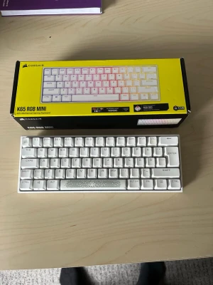 Corsair K65 RGB MINI tangentbord - Säljer ett vitt Corsair K65 RGB MINI mekaniskt tangentbord med kompakt 60% layout och RGB-belysning. Tangentbordet har nordisk layout och levereras i originalförpackning. Perfekt för gaming eller minimalistisk setup. Pris kan diskuteras vid snabb affär 
