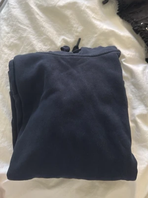 Mörkblå hoodie med dragsko - En enkel och stilren mörkblå hoodie med huva och dragsko. Hoodien är gjord i mjukt bomullsmaterial och har en klassisk passform utan tryck eller logga. Perfekt för en avslappnad look och lätt att matcha med andra plagg.
