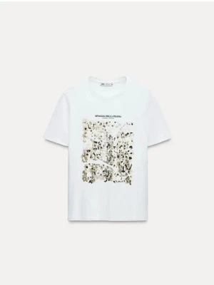 Vit t-shirt med abstrakt tryck Zara - Vit t-shirt från Zara med ett stort abstrakt tryck i guld svart och grå toner på bröstet. Texten 'SPIAGGIA DELLA PELOSA' står ovanför trycket. Klassisk passform och rund halsringning. Perfekt för en avslappnad stil, har några små defekter som går bort i tvätt!