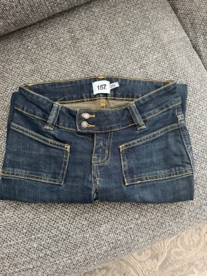 Mörklblåa jeans med fickor - Snygga mörkblå jeans med bootcut och dubbla knappar i midjan. Jeansen har fram- och bakfickor med kontrastsömmar i gult och är tillverkade i klassiskt denimtyg. Perfekta för en avslappnad och trendig look.