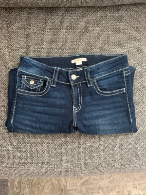 Mörkblå bootcut jeans med kontrastsömmar - Snygga mörkblå bootcut med vita kontrastsömmar och dekorativa fickor både fram och bak. Klassisk femficksmodell med silverfärgade knappar och detaljer. 