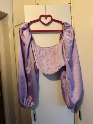 Missguided topp ljuslila strl XS - Topp med långa puffärmar och korsettinspirerad midja. Toppen har en fyrkantig halsringning och dragkedja baktill.