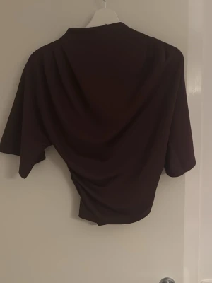 Vinröd åtsittande topp med kort ärm - Snygg vinröd topp med korta ärmar och draperad effekt i midjan. Toppen har en avslappnad passform och är tillverkad i ett mjukt, stretchigt material som känns skönt mot huden. Perfekt att styla med jeans eller kjol.
