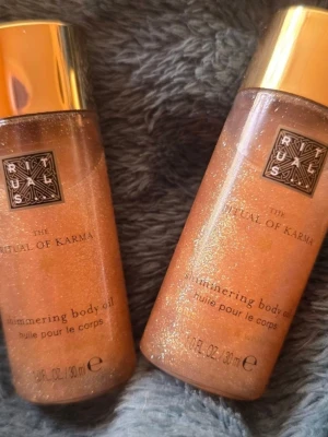 Rituals The Ritual of Karma Shimmering Body Oil - 2 st Shimmering body oil från Rituals, The Ritual of Karma. Oljan kommer i en genomskinlig plastflaska med guldlock och innehåller 30 ml. Ger huden en skimrande finish med gyllene glitter och har en lyxig känsla.