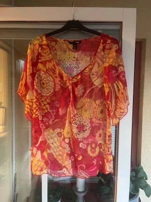 Blommig blus från H&M i mesh - Blus från H&M i transparent mesh med blommigt mönster i rött, rosa och gult. Storlek 34.