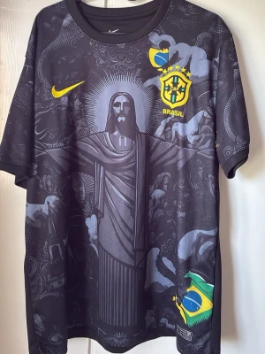 Nike Brasil svart t-shirt med tryck - Svart t-shirt från Nike med Brasil-logga och stort grafiskt tryck av Kristusstatyn och brasilianska flaggan. Gula detaljer och Nike Swoosh på bröstet. Tillverkad i lätt och ventilerande polyester, perfekt för dig som gillar snygga och unika sporttröjor.bra skick 8/10