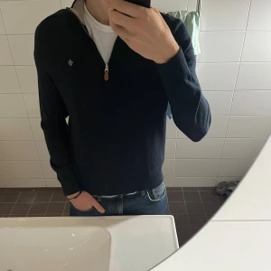 Mörkblå halvziptröja Morris - Snygg mörkblå stickad tröja från Morris med halfzip och liten broderad logga på bröstet. Tröjan har lång ärm, ribbade muddar och kontrastfärgad insida vid kragen. Perfekt till alla årstider. Har knappt använt den, som ny. Nypris 1800.