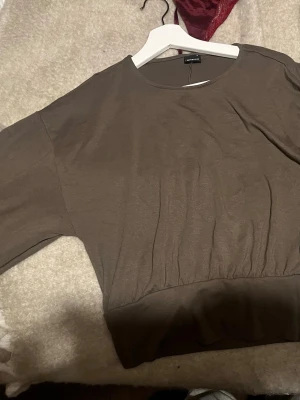 Brun loose topp från Gina tricot - Snygg brun topp från Gina tricot  med loose passform och bred resår i midjan. Toppen har rund halsringning och trekvartsärm, perfekt för en avslappnad och trendig look. Tillverkad i mjukt bomullsmaterial.