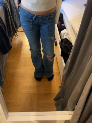 Blå slitna bootcut jeans från Gina Tricot  - Säljer ett par blå bootcut jeans med låg midja och slitningar på benen. .