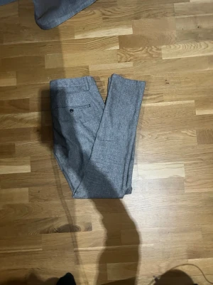 Grå kostymbyxor med dondup - Snygga grå kostymbyxor i klassisk rak modell med bälteshällor och en bakficka med knapp. Materialet ser ut att vara en mjuk och lite melerad textil som ger en stilren look. Perfekta till skjorta eller stickad tröja.