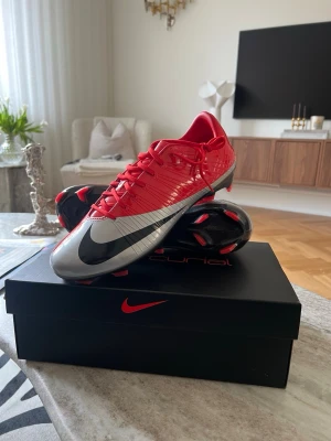 Nike Mercurial röda fotbollsskor - Snygga Nike Mercurial fotbollsskor i rött med silver och svart swoosh. Skorna har en strömlinjeformad design, låg profil och är tillverkade i syntetmaterial för bästa bollkontroll och grepp på planen. Perfekta för dig som vill sticka ut på fotbollsplanen.
