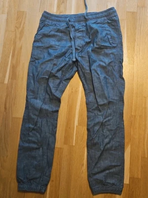 Blå byxor från Abercombrie and Fitch - Snygga blå byxor med avslappnad passform och resår i midjan samt dragsko. Byxorna har sidofickor och resår vid bensluten för en chill look. Perfekta för en casual stil och lätta att matcha med t-shirt eller hoodie.