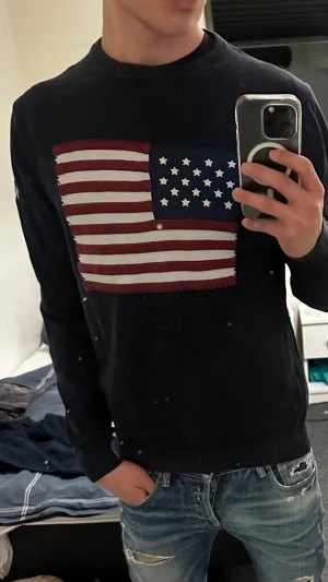 Mörkblå stickad USA gant tröja - Säljer en mörkblå stickad tröja från GANT med en stor amerikansk flagga framtill. Tröjan har rund hals, ribbade muddar och diskret GANT-text på ena ärmen. Perfekt för dig som gillar klassisk college-stil.