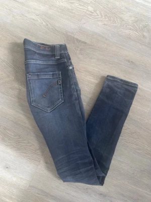 Mörgråa dondup jeans - Säljer ett par mörkgråa dondup  George jeans med  kontrastsömmar. Jeansen har klassiska fem fickor och en diskret detalj på bakfickan. Perfekt för dig som gillar en modern och tight passform.