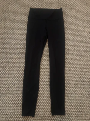 Svarta höga leggings Aimn - Snygga svarta leggings med hög midja och smal passform och lufthål på smalbenet. Perfekta till oversized tröjor eller crop tops. Stretchigt material som sitter skönt och följer kroppen. Klassisk modell utan synliga detaljer eller fickor.