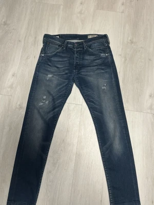 Mörkblå slitna jeans W32 L32 - Säljer ett par mörkblå jeans med lätt slitna detaljer och raka ben. Jeansen har klassisk femficksmodell och snygga tvättade partier framtill. Perfekta för en avslappnad och trendig look. Dem är slim fit så sitte rökte mer slimmat. Passar den som är ungefär 172-186 cm. 