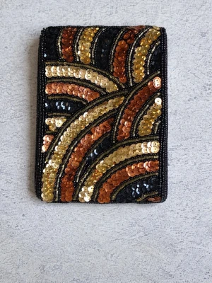 Kuvertväska med paljetter i guld och svart - Säljer en snygg kuvertväska med paljetter i guld, svart och koppar. Väskan har ett geometriskt mönster och är rektangulär i formen. Perfekt för dig som vill sticka ut med en glittrig accessoar. Materialet är tyg med paljettbroderi.