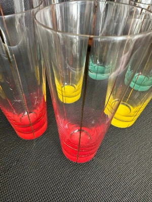 Färgglada höga glas med gulddetaljer - Säljer ett set med höga glas i klarglas med färgade bottnar i rött, gult och grönt. Glasen har tunna guldränder längs sidorna som ger en snygg retrovibe. Perfekta till dryck eller som dekoration i köket.