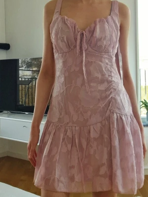 Rosa blommig klänning - Supersöt rosa kortklänning med blommigt mönster och volang nertill. 🌸 Säljer då den tyvärr inte kommit till användning då den var lite stor i bysten för mig. Prislapp kvar!