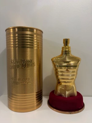 Jean Paul Gaultier Le Male Absolu 125ml - Lyxig parfym i form av en guldig torso från Jean Paul Gaultier, Le Male Absolu. Flaskan har en unik, maskulin design i metall och kommer med en matchande guldfärgad cylinderförpackning och röd sammetsbas. Perfekt för dig som gillar exklusiva dofter och snygg inredningsdetalj.